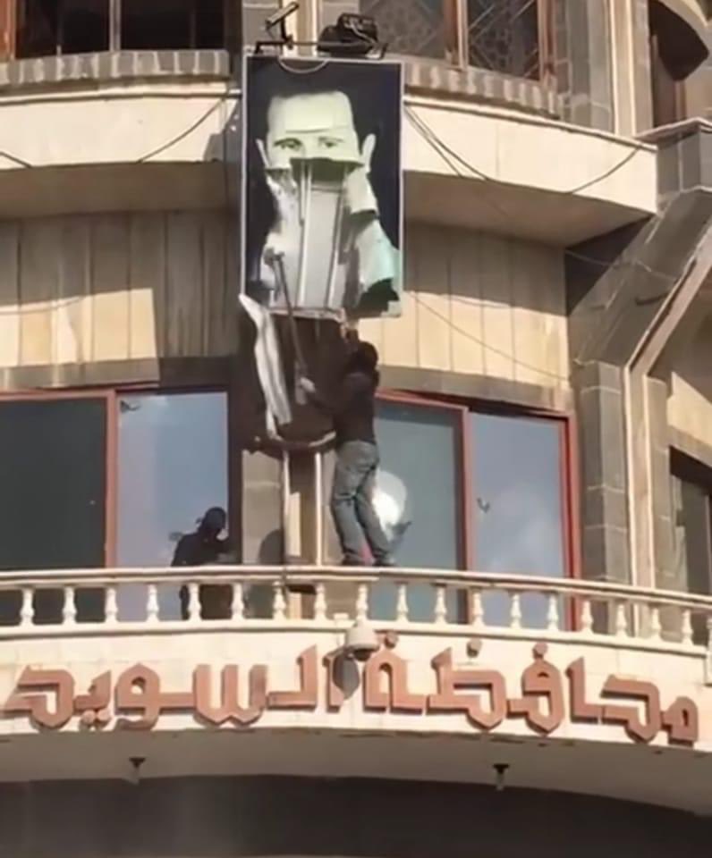 A protester removes a portrait of Bashar Assad from the Municipal Building in Suwayda city. Photo shared by activists on social media.